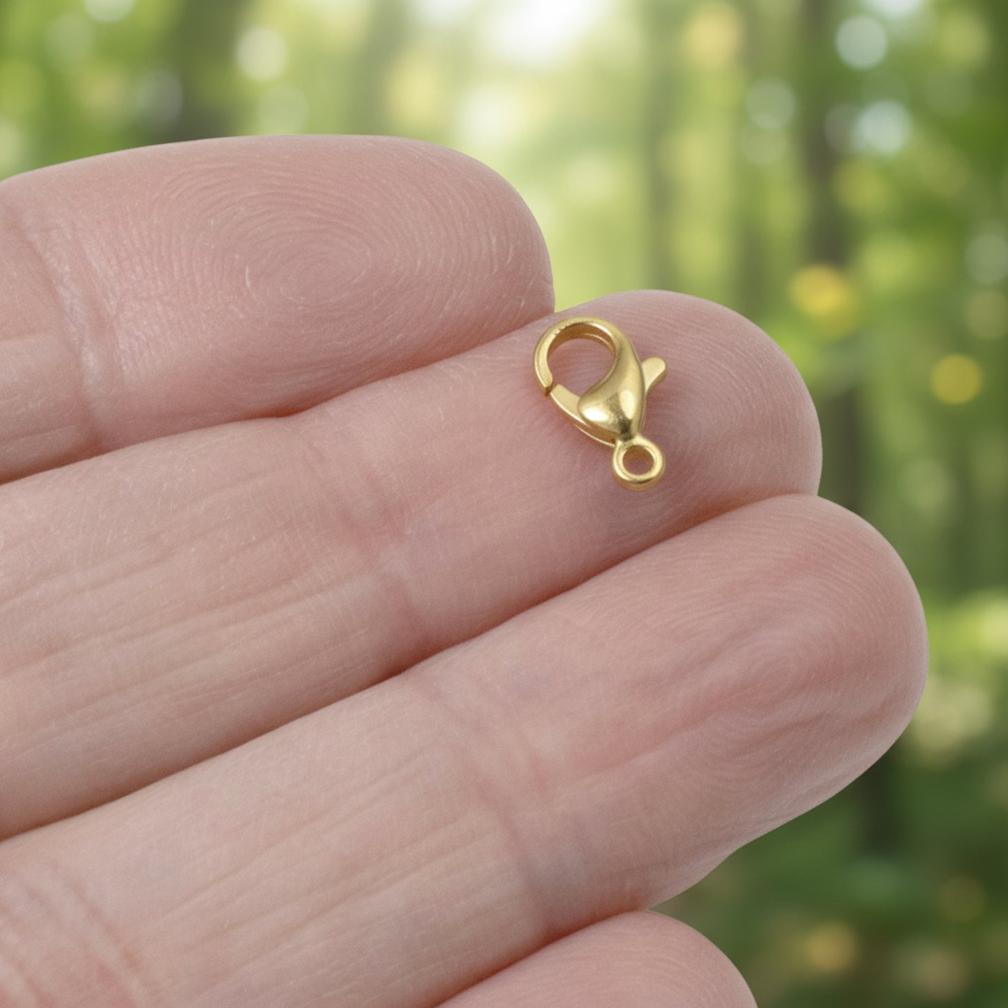 Hackberry Creek 18k gold-plated stainless steel lobster claw clasp held on a finger for scale