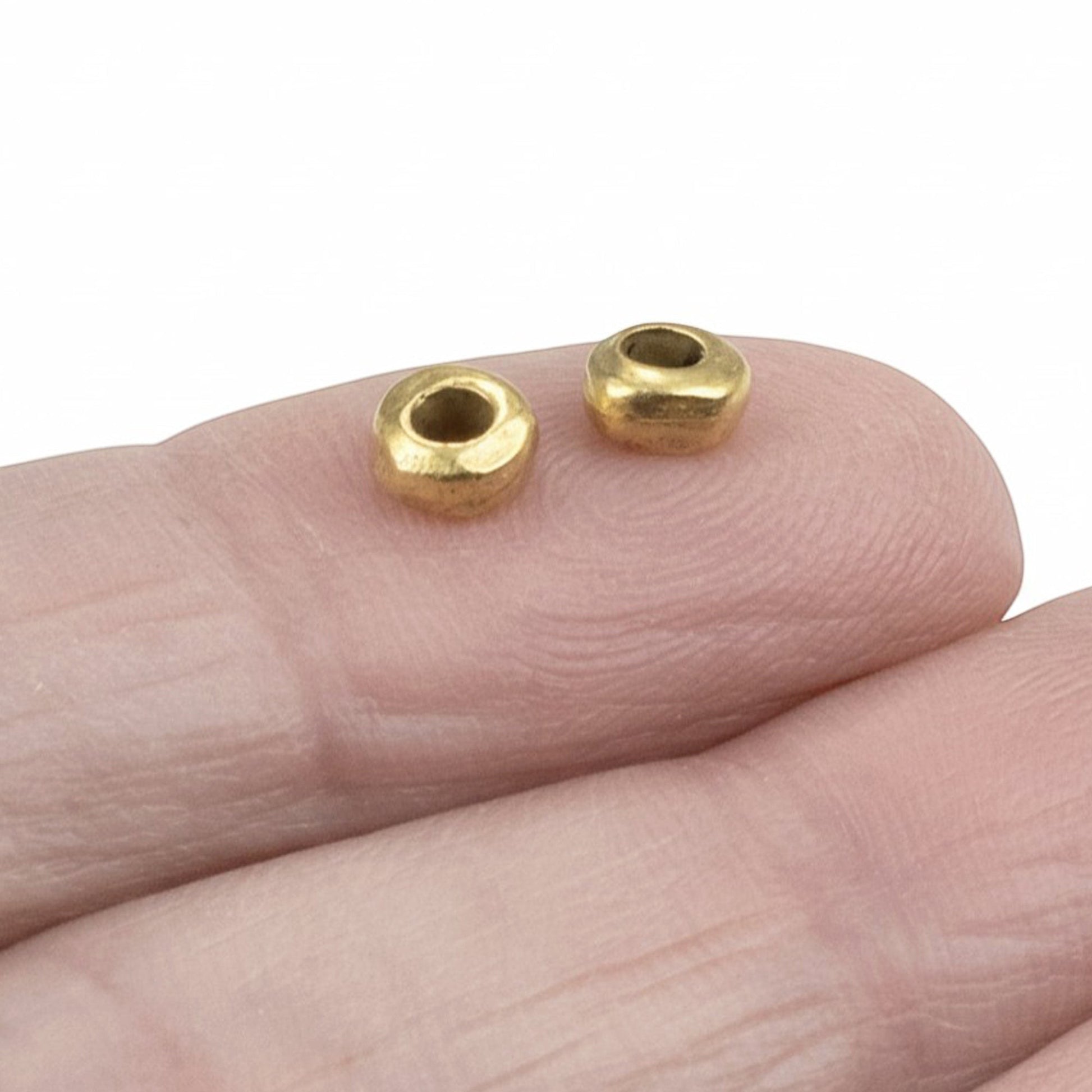 Hackberry Creek 24k gold plated pewter nugget spacer beads with organic shape on a finger for scale.
