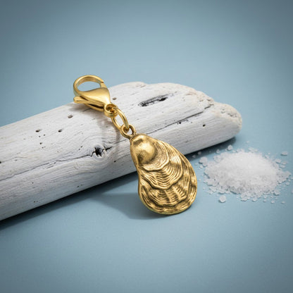 Hackberry Creek 24k gold-plated oyster shell charm with a lobster clasp, displayed on driftwood with sea salt.