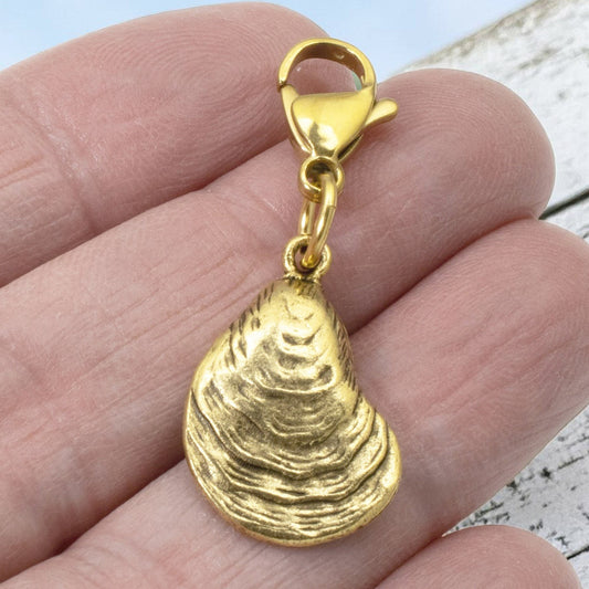 Hackberry Creek 24k gold-plated pewter oyster shell charm with a lobster clasp held in a hand.