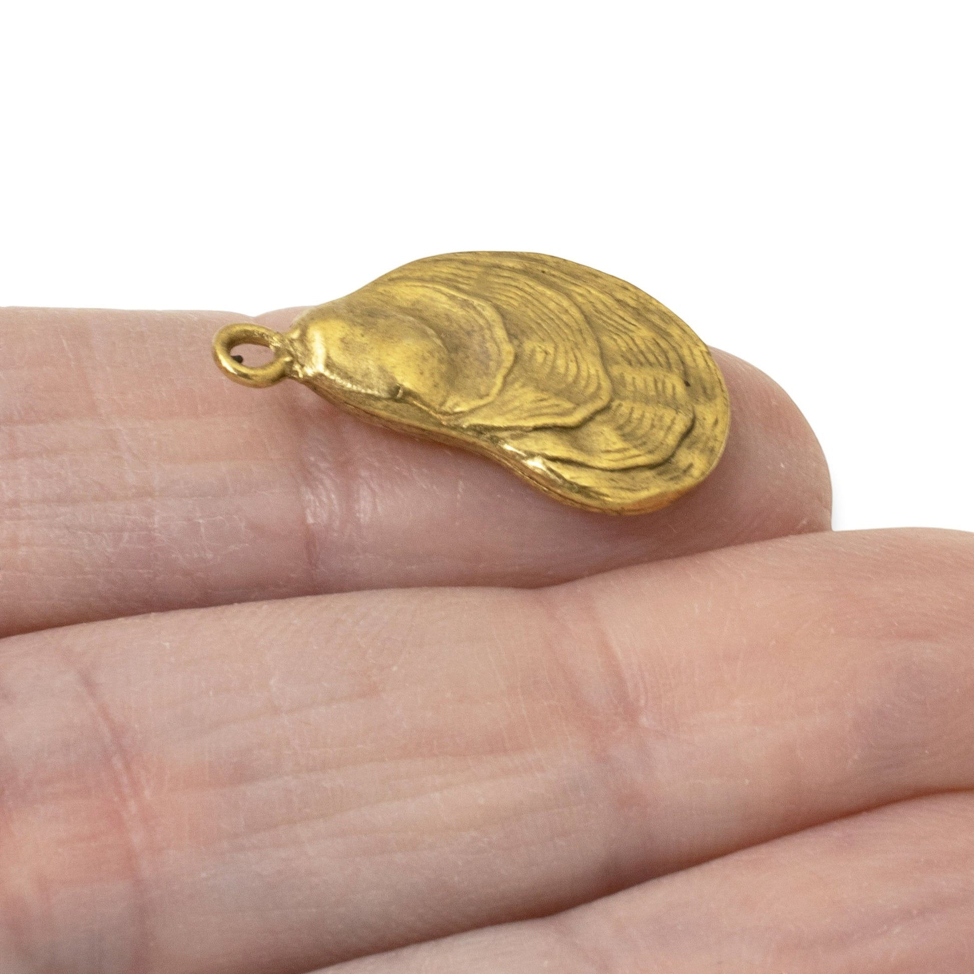 Hackberry Creek 24k gold plated oyster shell charm held on a finger, featuring detailed textured coastal design.