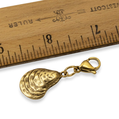 Hackberry Creek 24k gold-plated pewter oyster shell charm with a stainless steel lobster clasp next to a ruler.