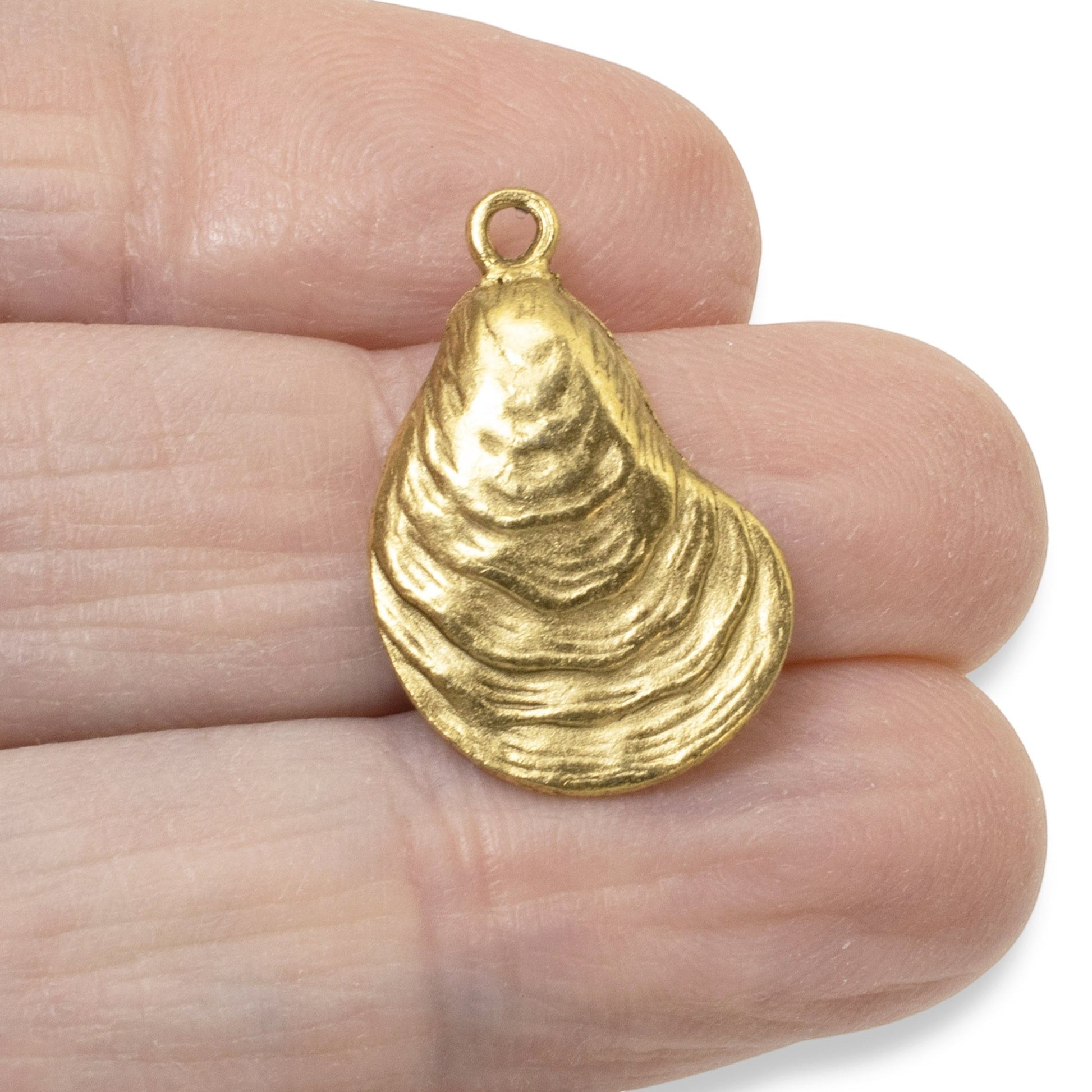 Hackberry Creek 24k gold plated oyster shell charm held between fingers for scale