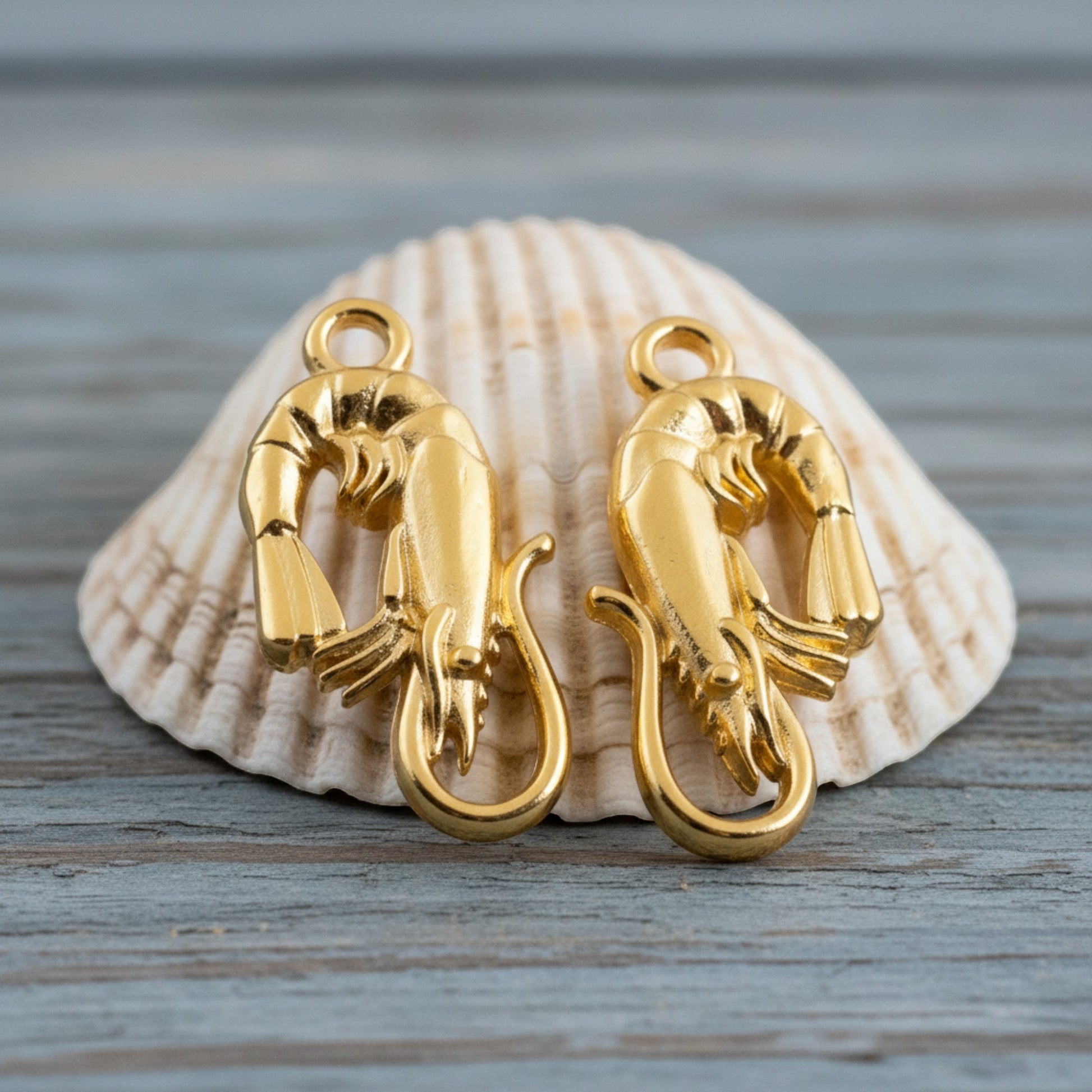 Hackberry Creek two 24K gold plated shrimp charms with detailed sculpting, displayed on a seashell.
