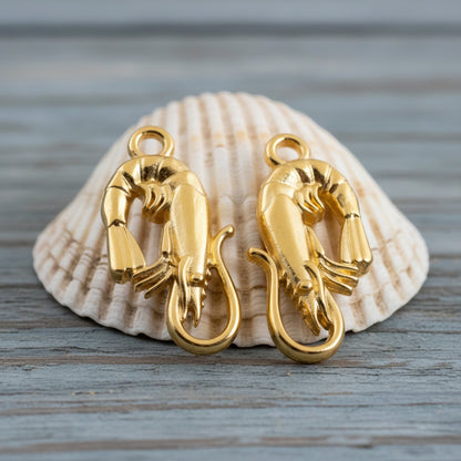 Hackberry Creek two 24K gold plated shrimp charms with detailed sculpting, displayed on a seashell.
