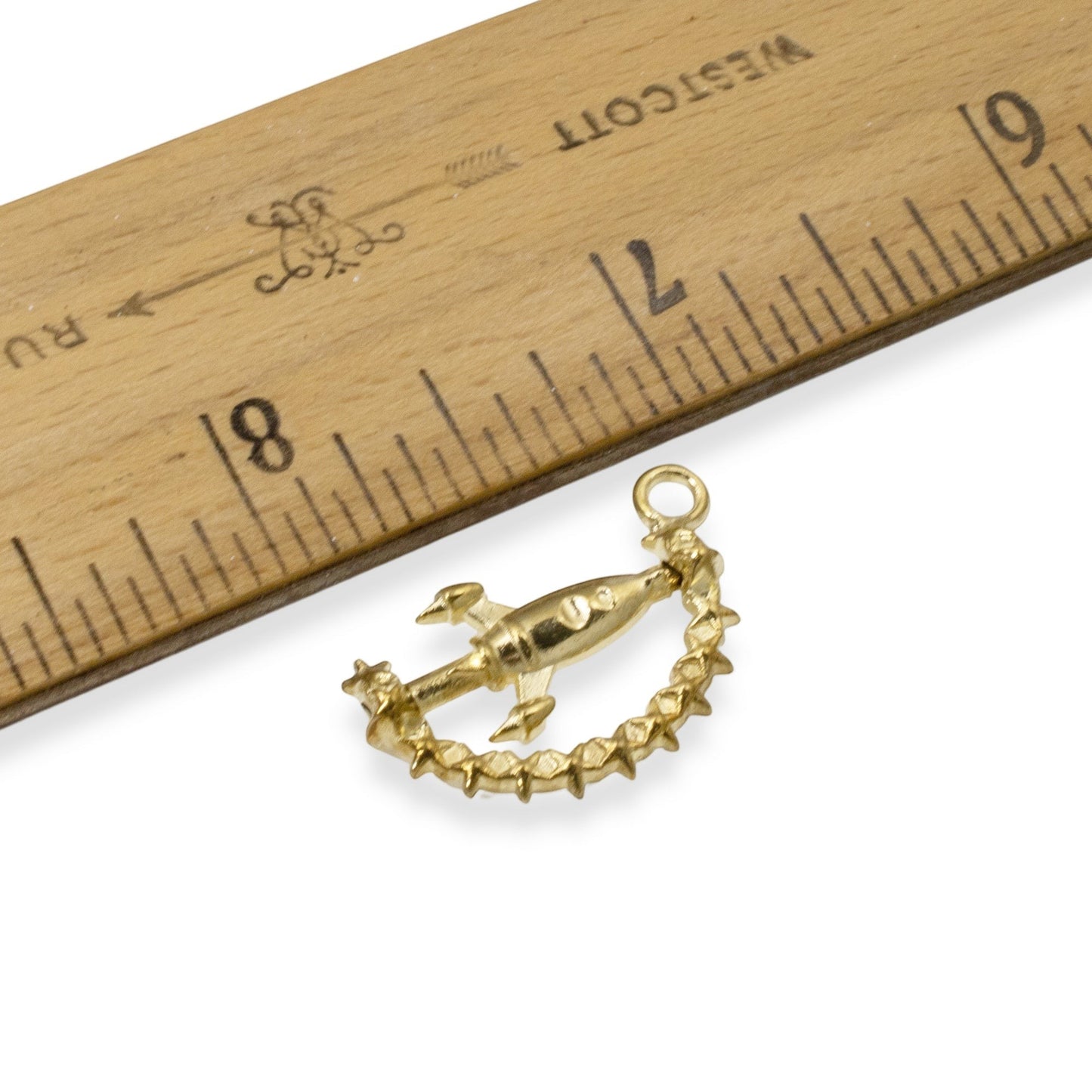 Hackberry Creek gold alloy spinning rocket charm with star details next to a wooden ruler for size reference.