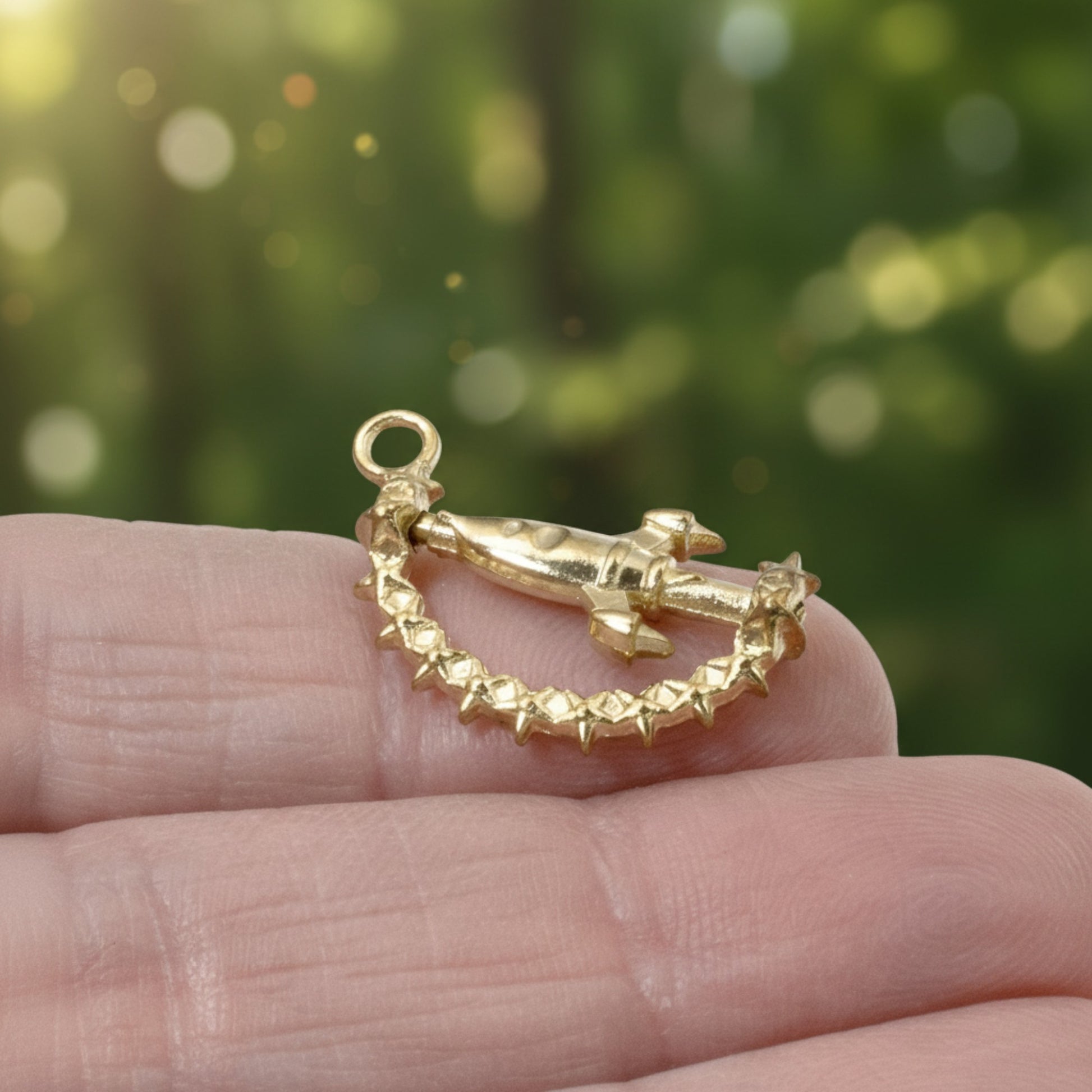 Hackberry Creek gold spinning rocket charm with star details held in a hand against a blurred green background