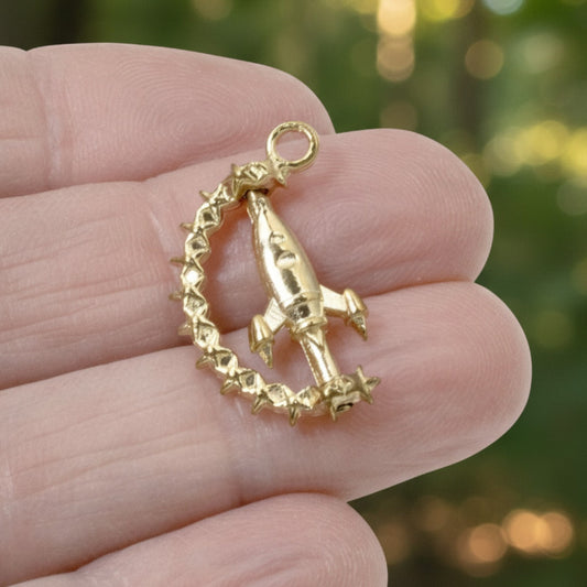 Hackberry Creek gold alloy spinning rocket charm with star details held in a hand against a blurred green background.