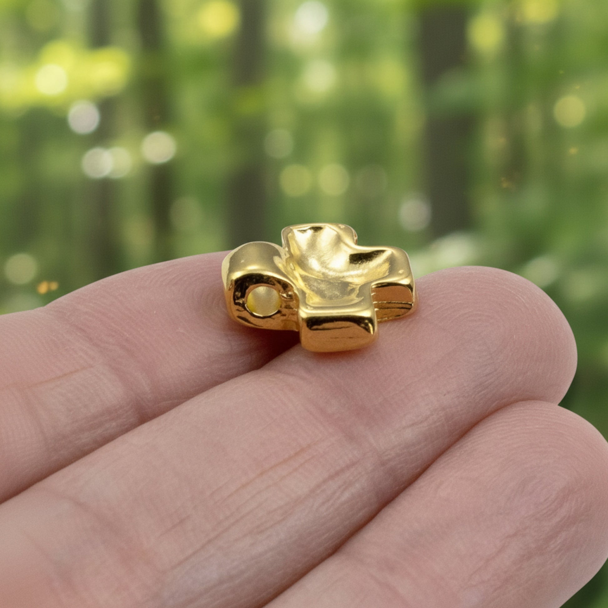 Hackberry Creek 24K gold plated cross pendant with a textured wave surface held between fingers