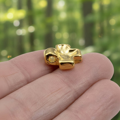 Hackberry Creek 24K gold plated cross pendant with a textured wave surface held between fingers