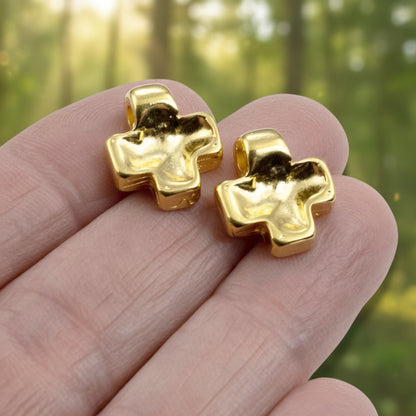 Hackberry Creek 24K gold plated cross pendants with textured wave surface held in hand against a blurred forest background