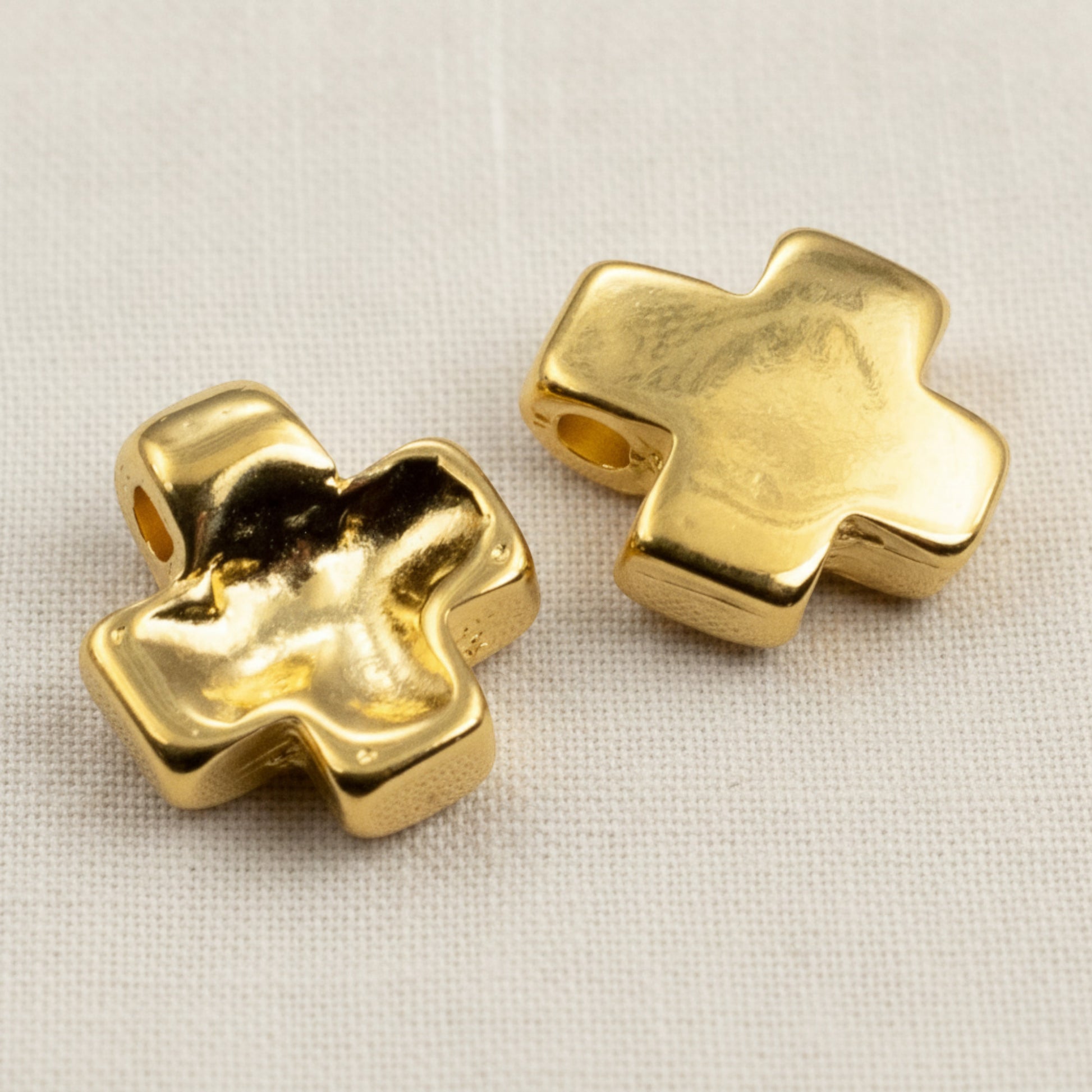 Hackberry Creek 24K gold plated cross pendants with textured wave surfaces for jewelry making on a white fabric base.