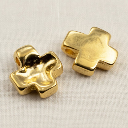 Hackberry Creek 24K gold plated cross pendants with textured wave surfaces for jewelry making on a white fabric base.