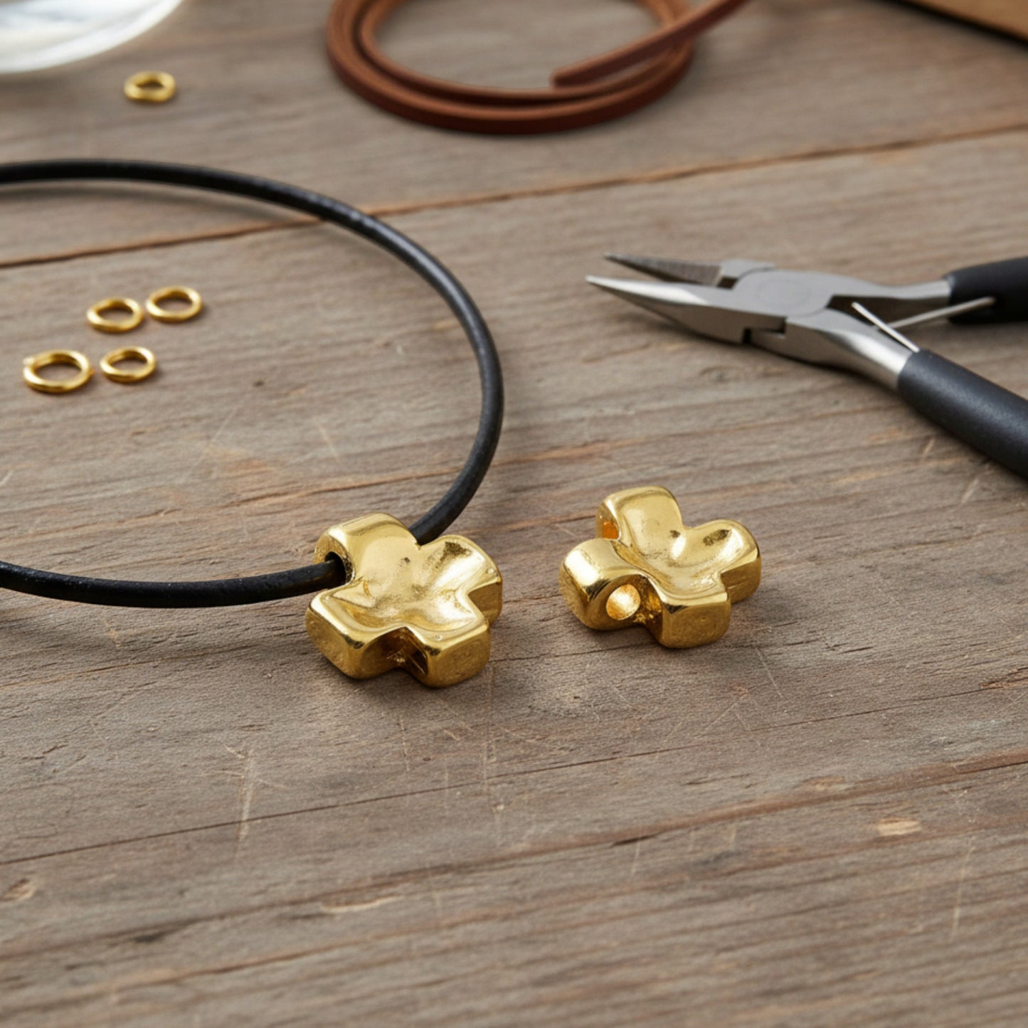 Hackberry Creek 24K gold plated textured cross pendants for jewelry making on a rustic wooden table with tools