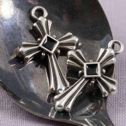 Hackberry Creek silver plated gothic cross pendants with black enamel centers on a metal spoon background