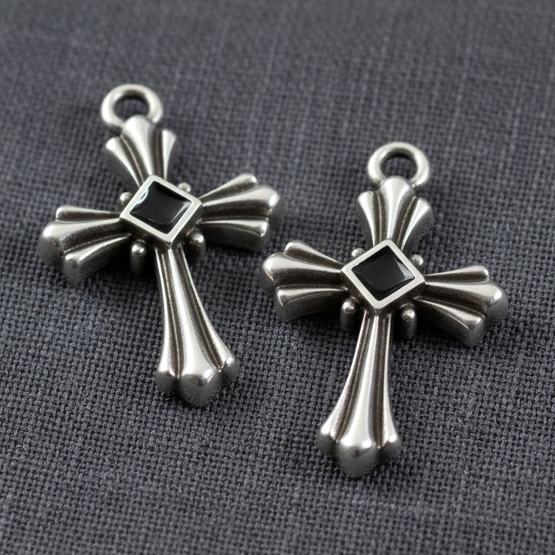 Hackberry Creek silver plated gothic cross pendants with black enamel center accents on a grey fabric background