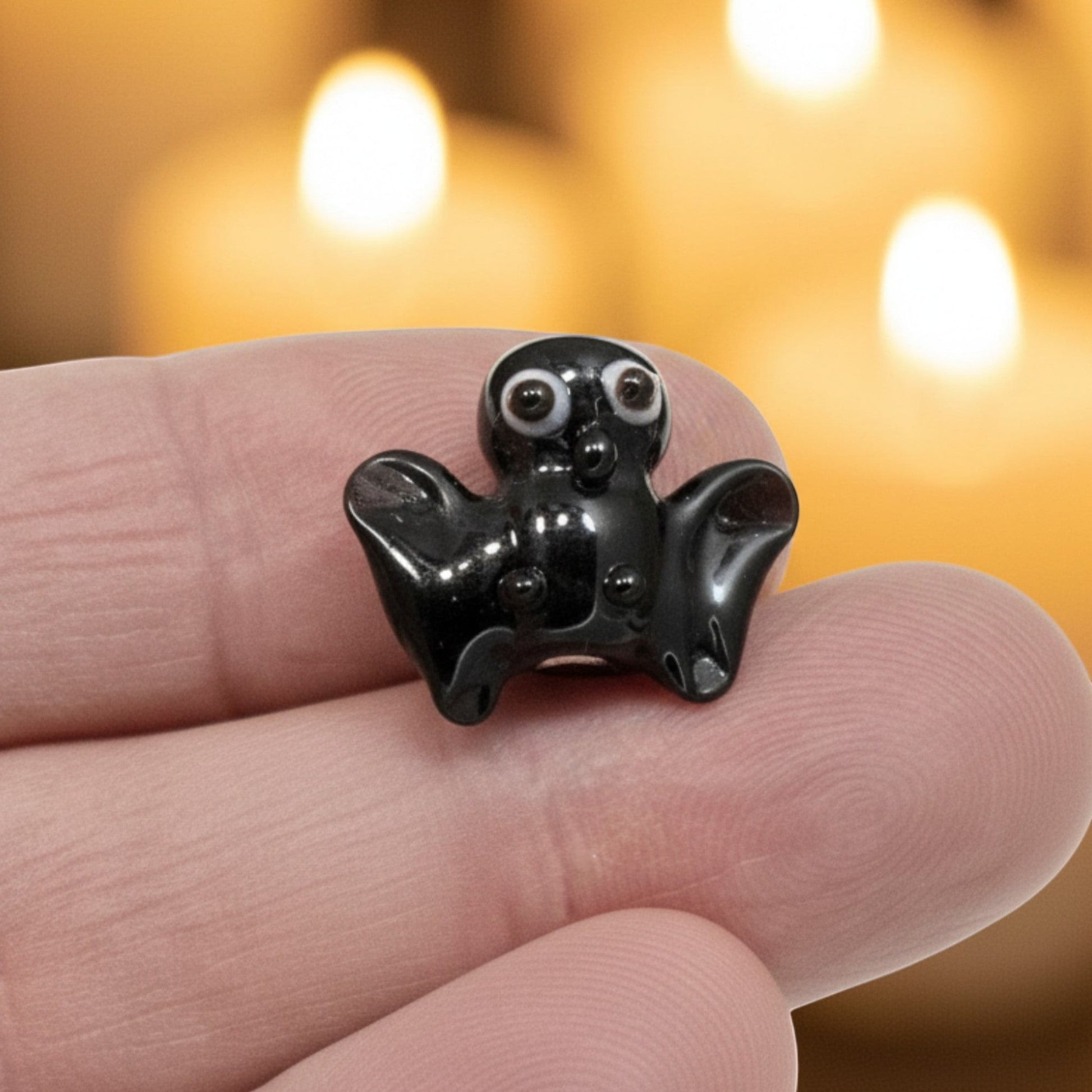 Hackberry Creek handmade lampwork glass bat bead in black with detailed eyes held against a candlelit background