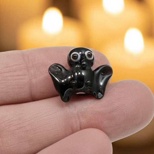 Hackberry Creek handmade lampwork glass bat bead in black with detailed eyes held against a candlelit background