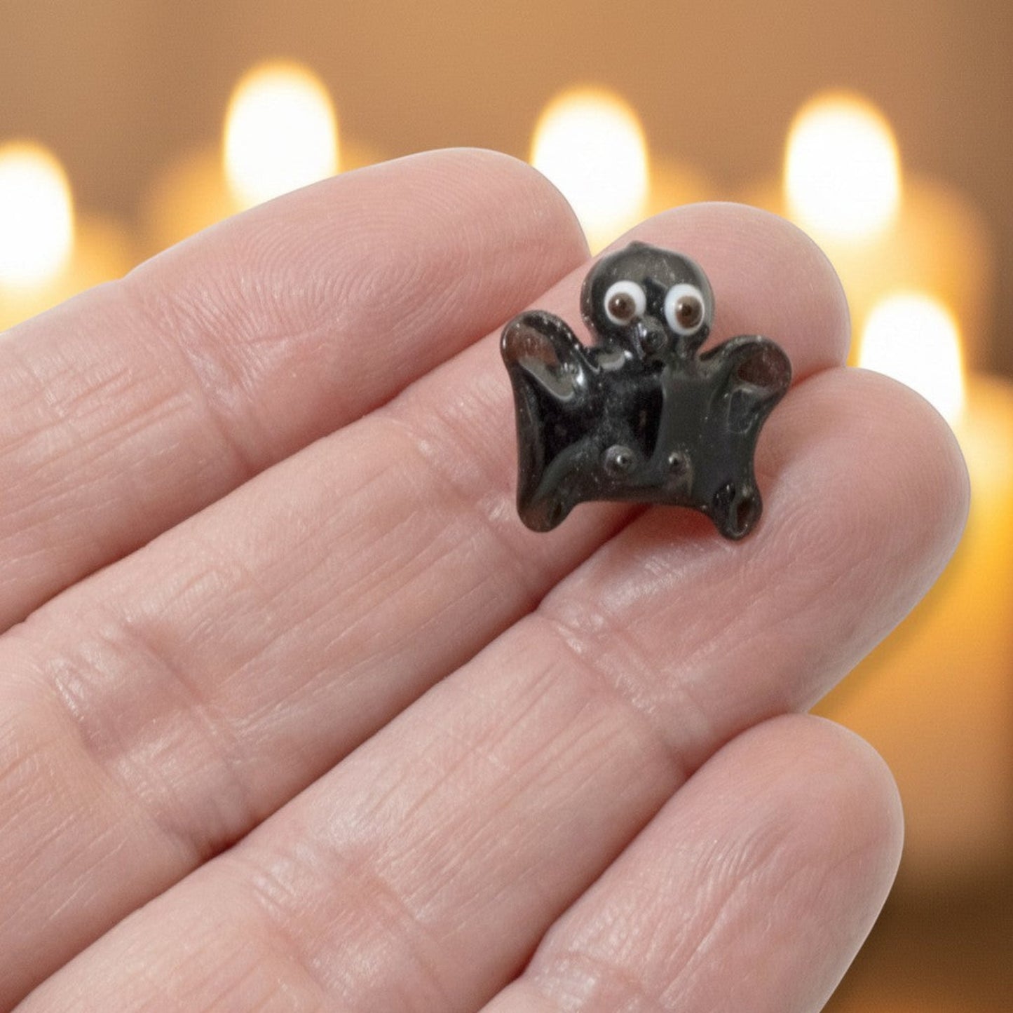 Hackberry Creek handmade black lampwork glass bat bead with detailed white and brown eyes held in a hand.