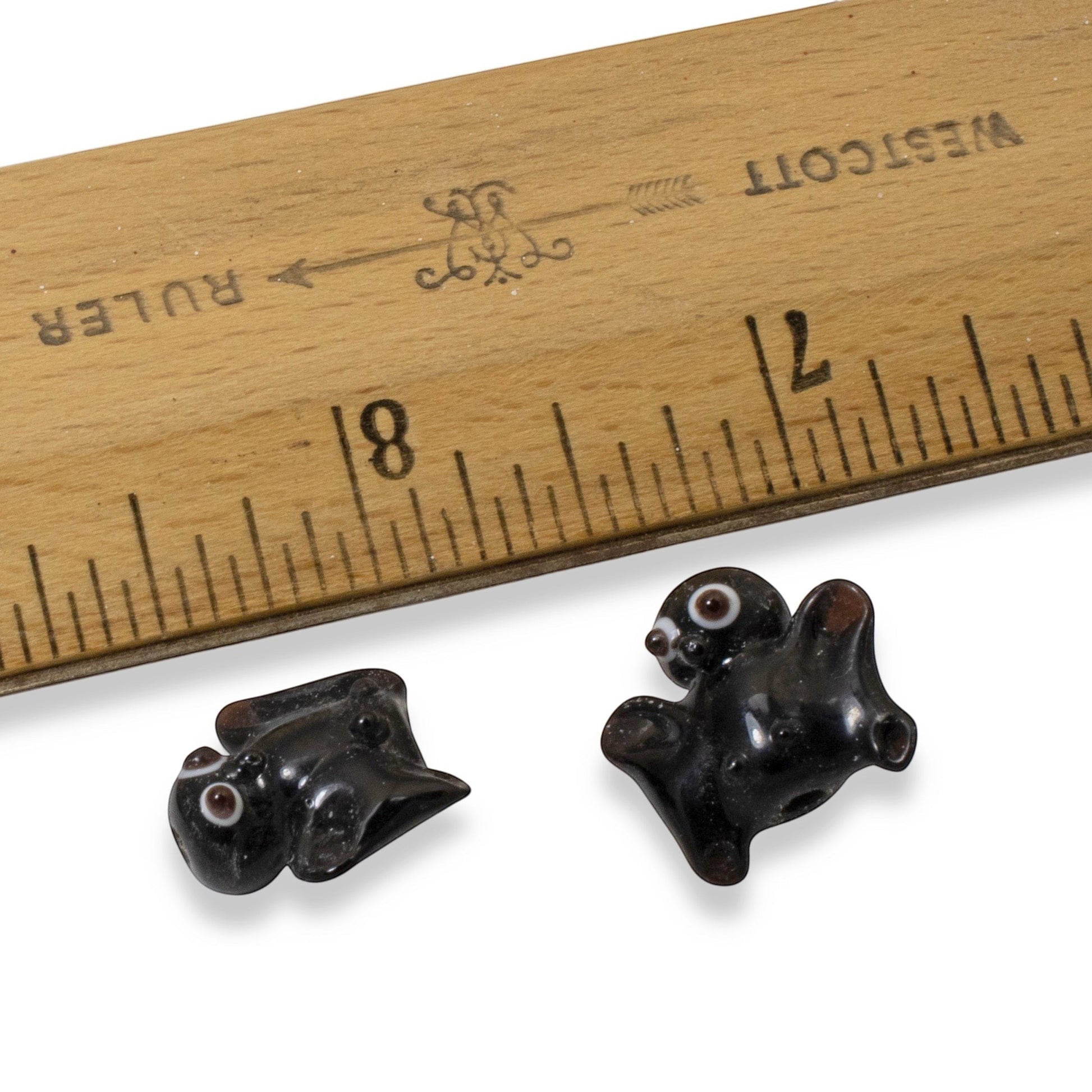 Hackberry Creek handmade black lampwork glass bat beads with detailed eyes next to a wooden ruler for scale
