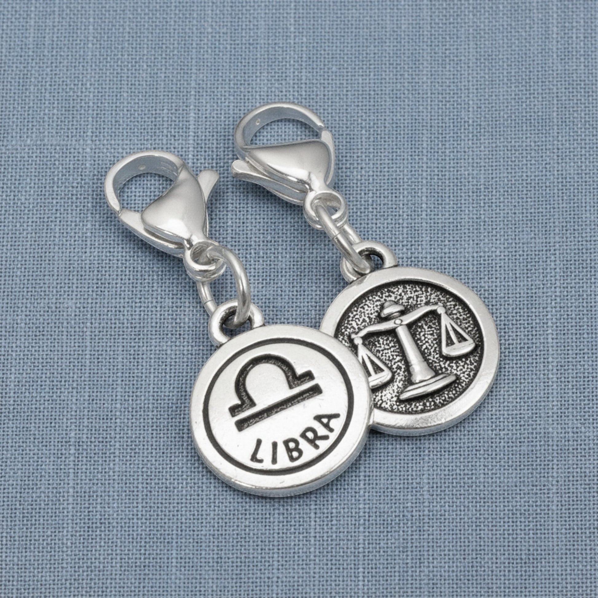 Hackberry Creek silver Libra zodiac charm with lobster clasp showing the scales symbol and Libra text on blue fabric