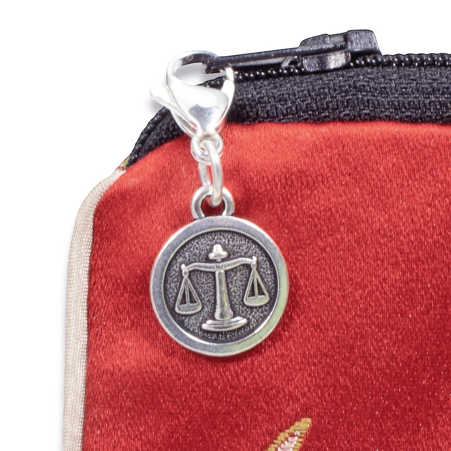 Hackberry Creek silver Libra zodiac scales charm with stainless steel lobster clasp attached to a red zipper pouch.