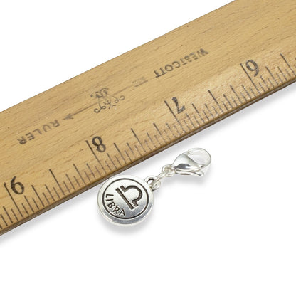 Hackberry Creek silver Libra zodiac charm with lobster clasp next to a wooden ruler for scale