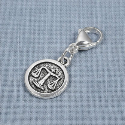 Hackberry Creek silver Libra zodiac charm with scales design and stainless steel lobster clasp on blue fabric.