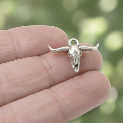 Hackberry Creek silver longhorn steer skull charm held between fingers, featuring antique oxidized silver finish.