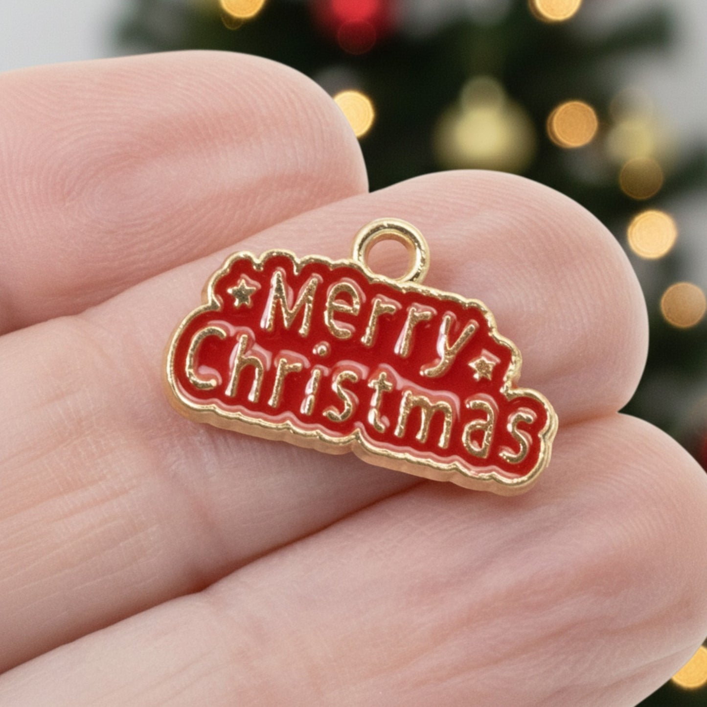 Hackberry Creek gold-plated metal alloy charm with red enamel Merry Christmas text held between fingers