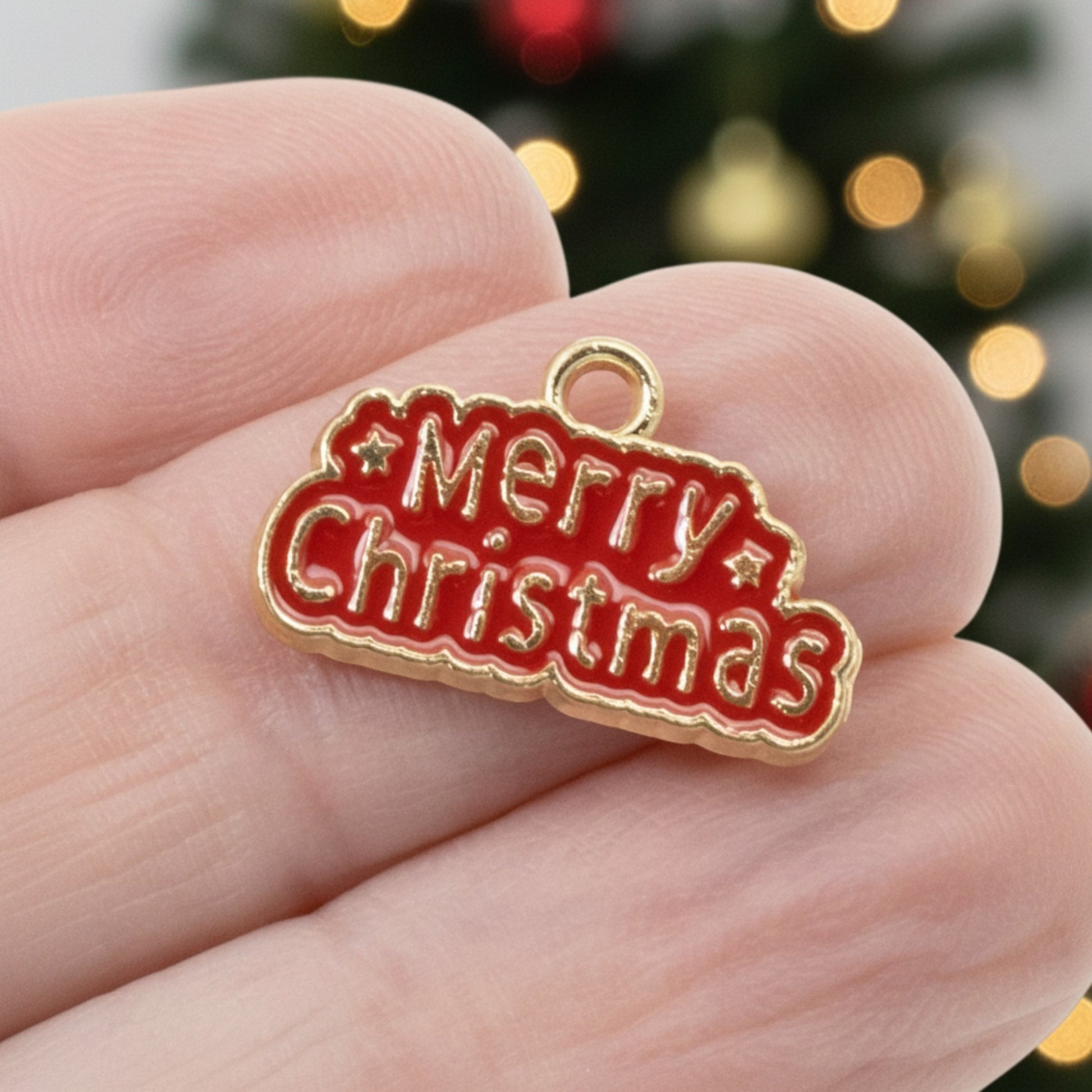 Hackberry Creek gold-plated metal alloy charm with red enamel Merry Christmas text held between fingers