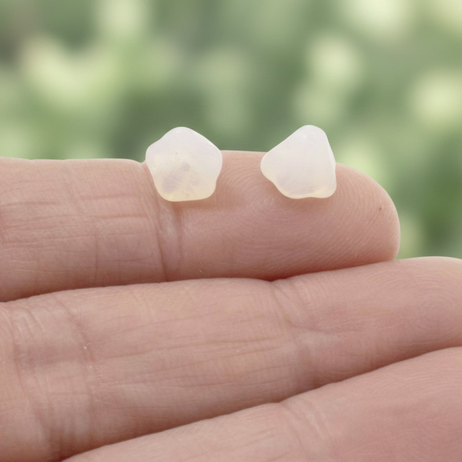 Hackberry Creek milky white Czech glass bell flower beads for jewelry making held on a finger