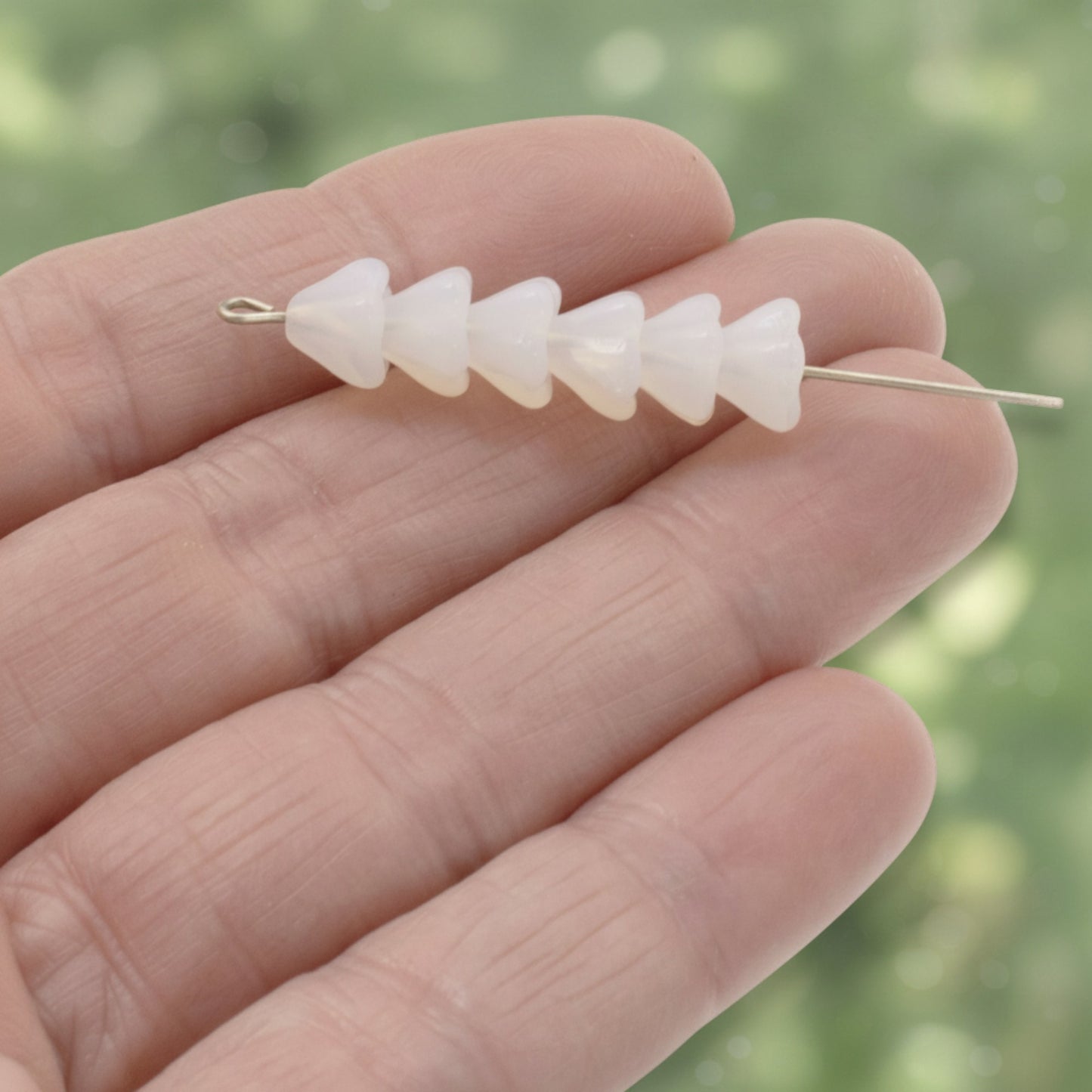 Hackberry Creek milky white Czech glass bell flower beads on a wire held in a hand for jewelry making.