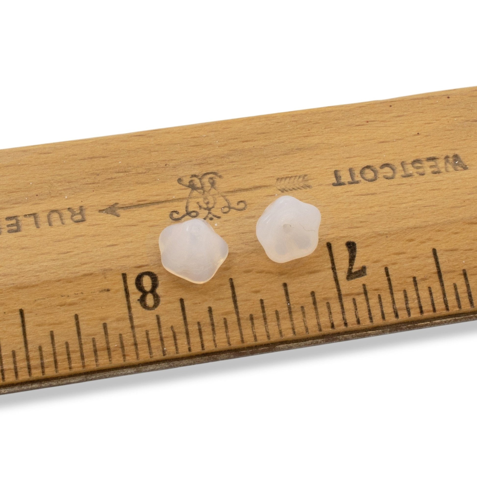 Hackberry Creek milky white Czech glass bell flower beads for jewelry making, shown next to a ruler for scale.