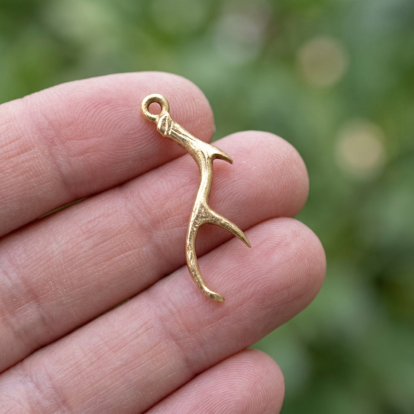 Hackberry Creek Nunn Design antique gold plated pewter antler charm held between fingers for jewelry making