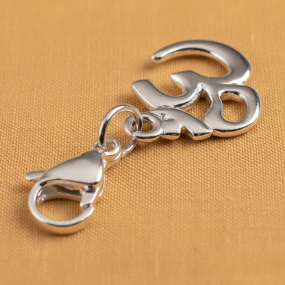 Hackberry Creek Om symbol charm in white bronze finish with a silver-plated lobster clasp on a textured gold background