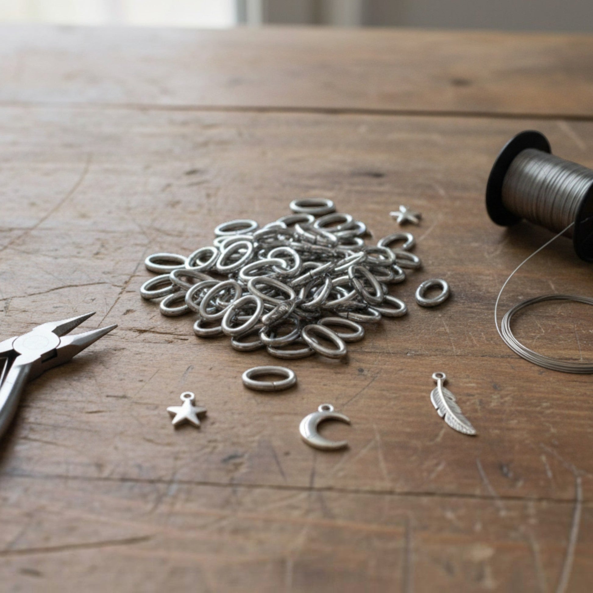 Hackberry Creek heavy duty dark silver 304 stainless steel oval jump rings on a wooden table with jewelry tools