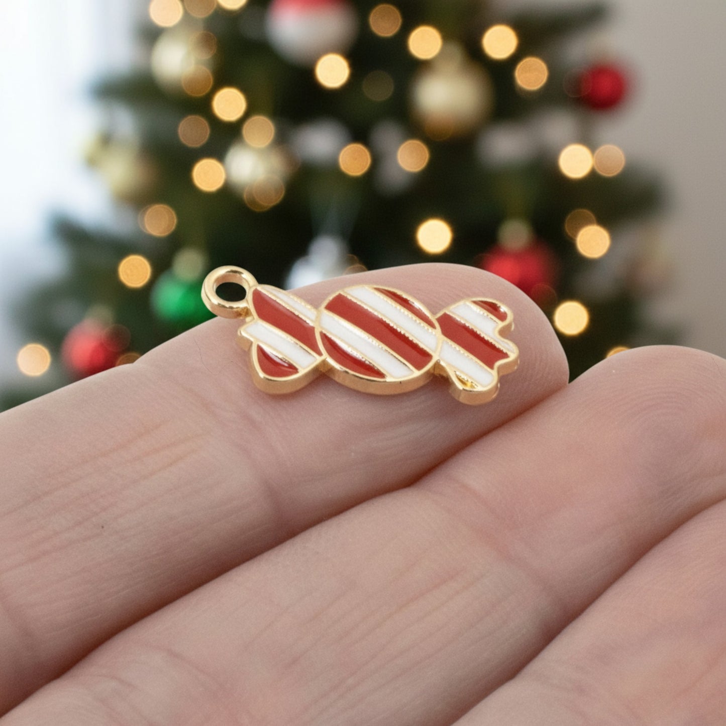 Hackberry Creek peppermint candy charm with red and white enamel stripes and gold-plated backing held in hand