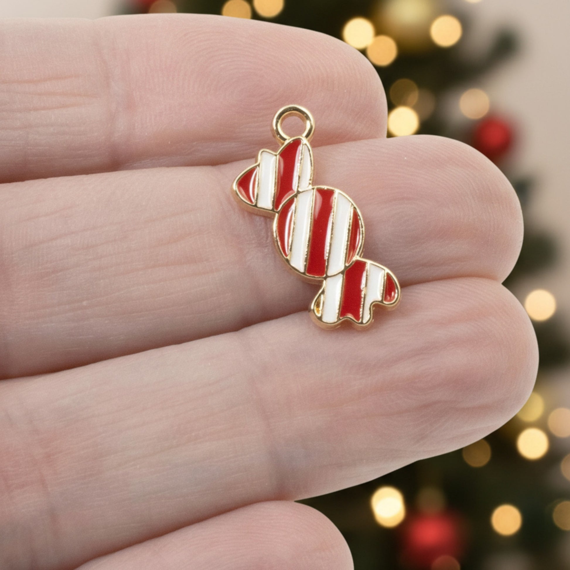 Hackberry Creek peppermint candy charm with red and white enamel stripes and gold-plated backing held in hand.