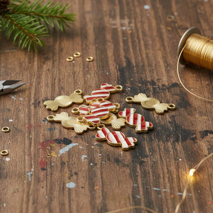 Hackberry Creek peppermint candy charms with red and white enamel and gold-plated backing on a rustic wooden table.