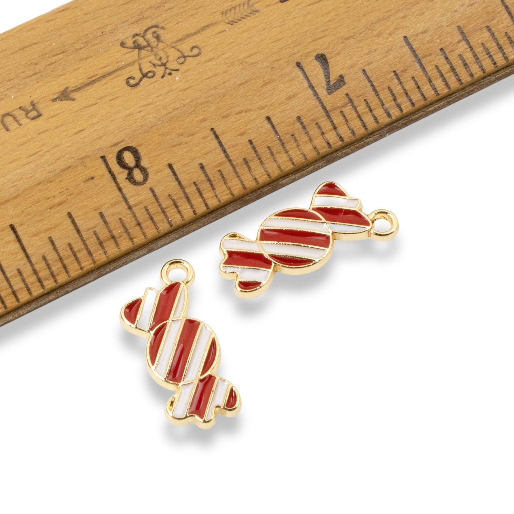 Hackberry Creek peppermint candy charms with red and white enamel and gold-plated backing next to a wooden ruler.