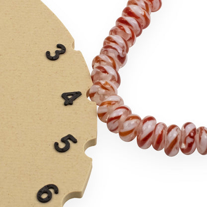 Hackberry Creek red and white peppermint stripe glass rondelle beads on a measuring tool for jewelry making