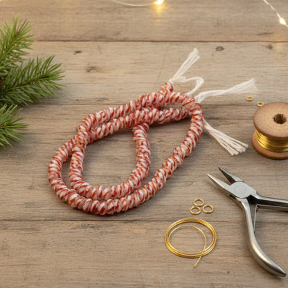 Hackberry Creek red and white peppermint stripe glass rondelle beads on a wooden table with jewelry making tools.