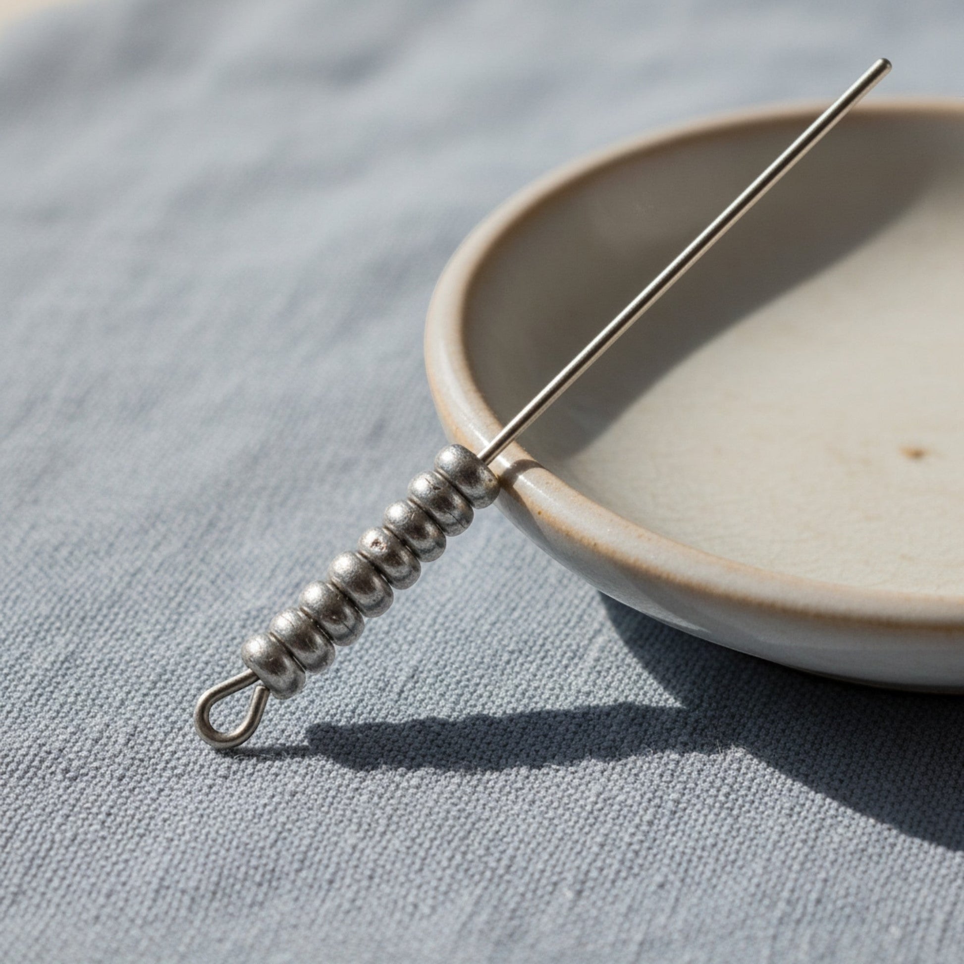 Hackberry Creek Pewter 3mm smooth heishi disk spacer beads on a needle tool, neutral tone.