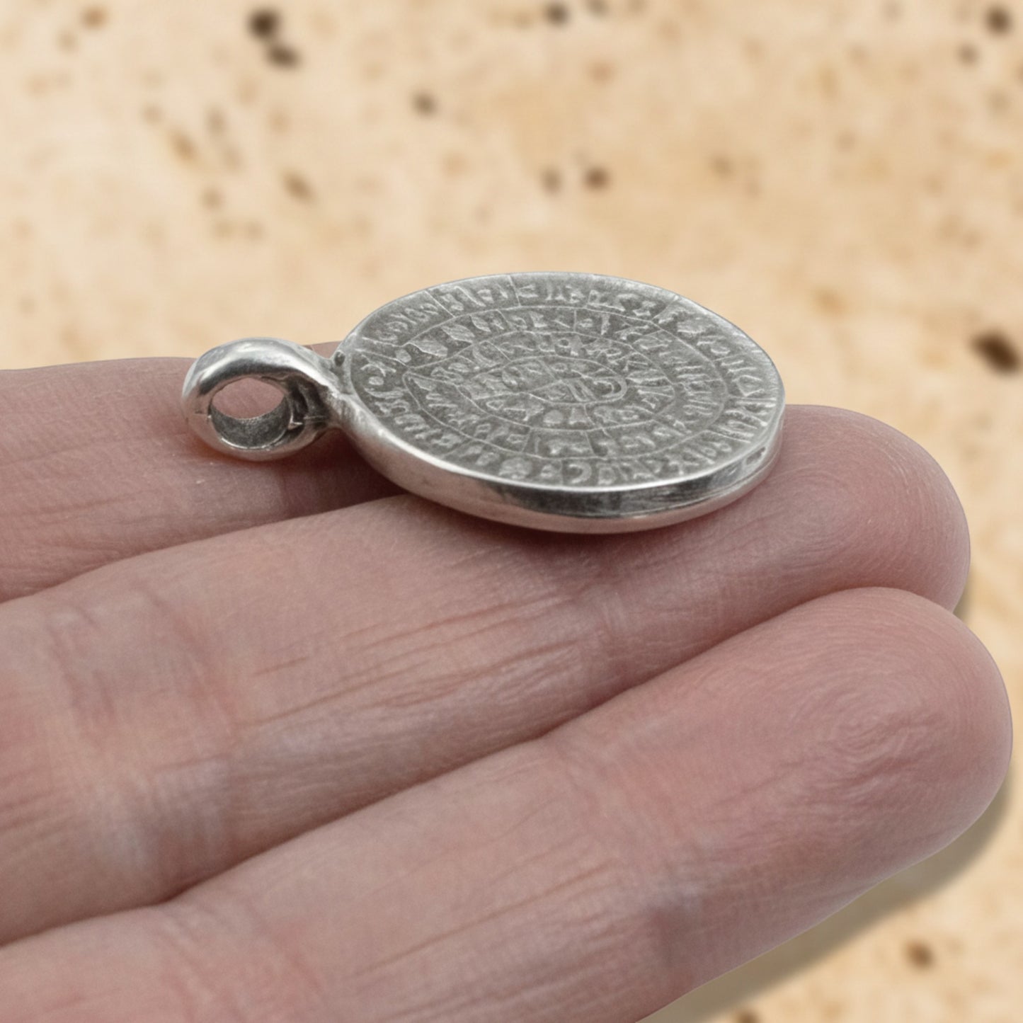 Hackberry Creek silver plated Zamak Phaistos Disc pendant with spiral script, 25mm oval shape, made in Greece.