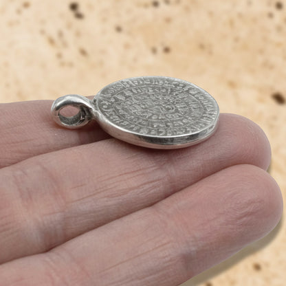Hackberry Creek silver plated Zamak Phaistos Disc pendant with spiral script, 25mm oval shape, made in Greece.