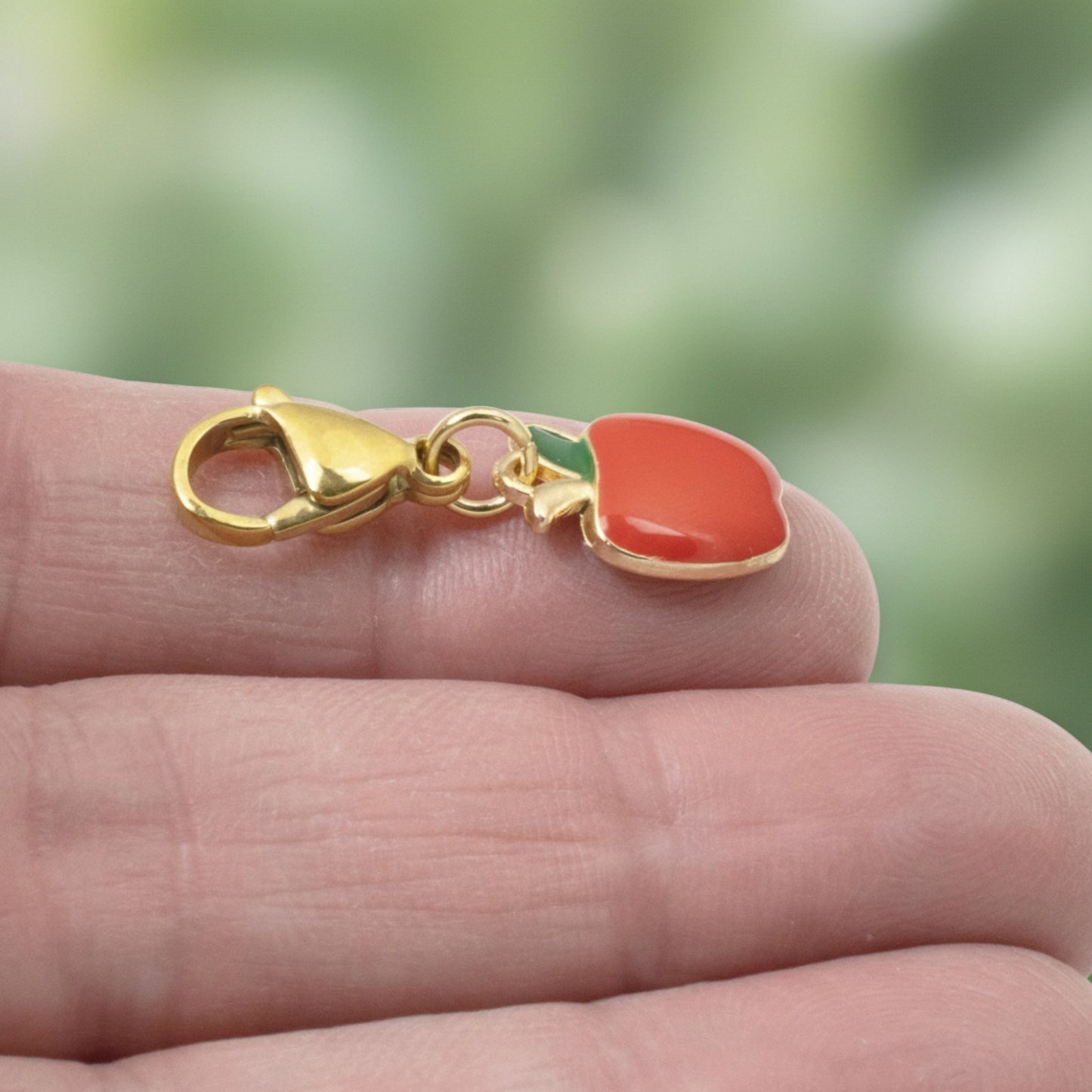 Hackberry Creek red apple charm with green enamel leaf on a gold-plated brass clasp held in hand