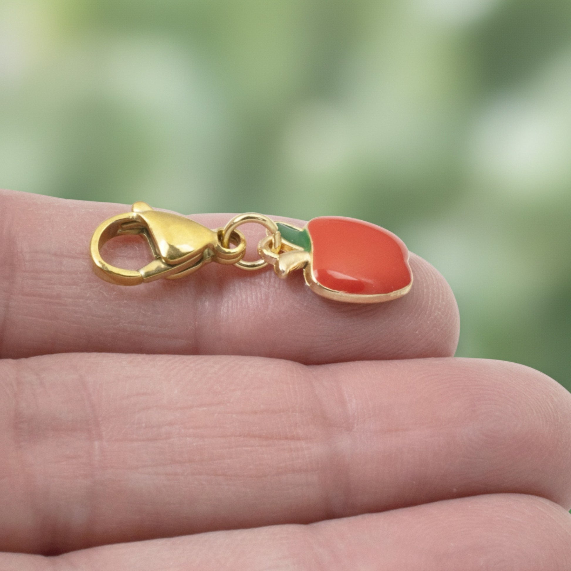 Hackberry Creek red apple charm with green enamel leaf on a gold-plated brass clasp held in hand