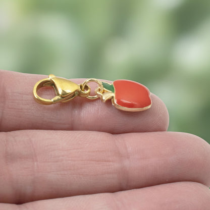 Hackberry Creek red apple charm with green enamel leaf on a gold-plated brass clasp held in hand