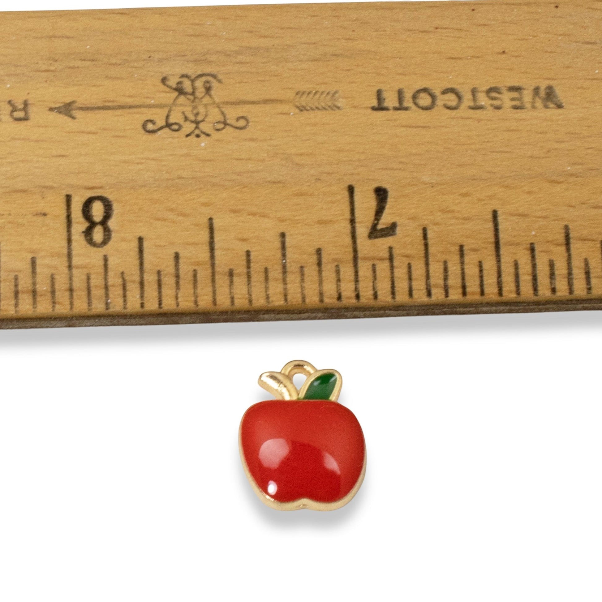 Hackberry Creek apple charm with glossy red enamel and green leaf detail next to a ruler for size reference